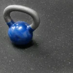 Blue kettlebell resting on a black speckled rubber gym mat.